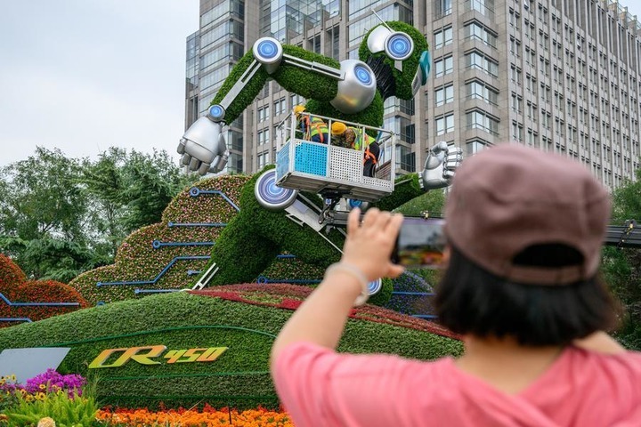 A woman takes pictures of a set of floral decorations under construction at Dongdan area along Chang'an Avenue in Beijing, capital of China, Sept. 25, 2026. Floral decorations have been set up along the Chang'an Avenue in Beijing ahead of China's National Day holidays. (Xinhua/Hu Jingwen)